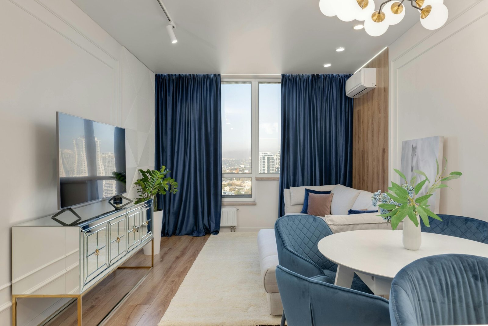 Stylish living room featuring blue velvet curtains, white furniture, and city view.